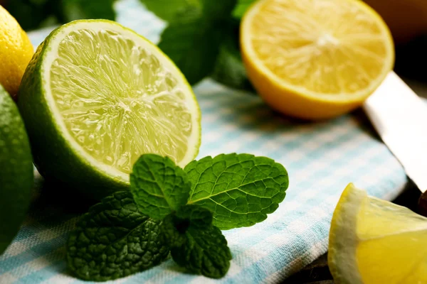 Limone fresco affettato e lime con foglie verdi sul primo piano del tovagliolo blu — Foto Stock