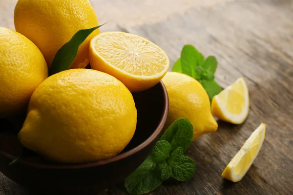 Свежие лимоны с зелеными листьями в миске на деревянном фоне — стоковое фото
