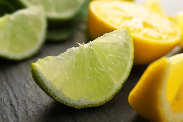 Rodajas de limón fresco y lima con hojas verdes en primer plano de la mesa —  Fotos de Stock