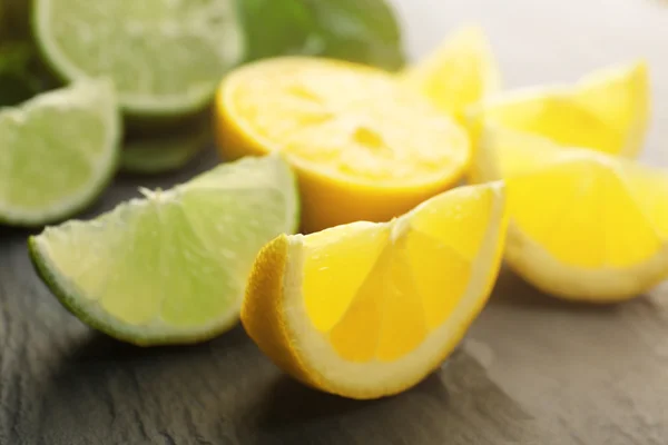 Slices of fresh lemon and lime with green leaves on table closeup — Stock Photo, Image