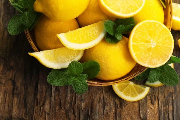 Fresh lemons with green leaves in bowl on wooden table, top view — Stock Photo, Image