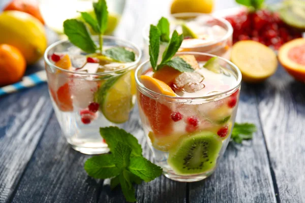 Refreshing cocktails with ice, mint, pomegranate seeds and slices of fruits on wooden background