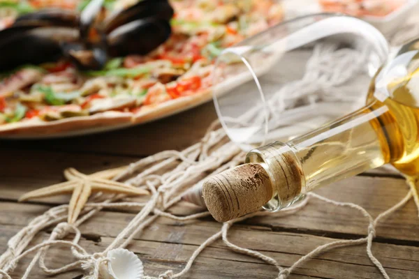 Pizza met zeevruchten, rode paprika, groene olijven en fles wijn op houten tafel — Stockfoto