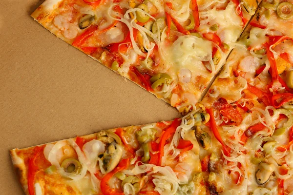 Pizza tranchée aux fruits de mer, poivron rouge et olives vertes dans une boîte en carton, gros plan — Photo
