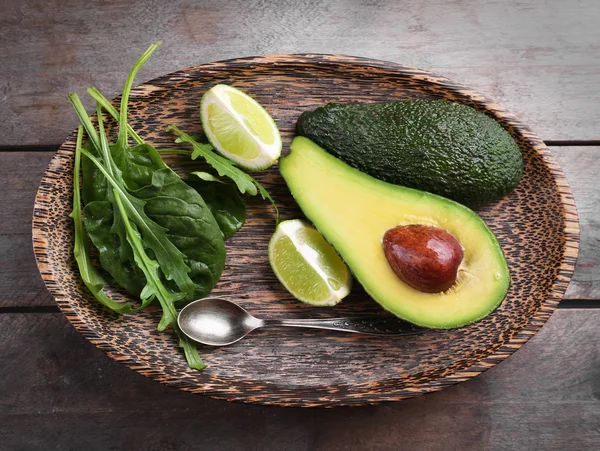 Sliced avocado with lime, spinach and arugula on wooden plate — Stock Photo, Image