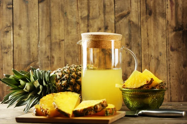 Ananas segmenten en SAP in glaswerk op houten tafel — Stockfoto