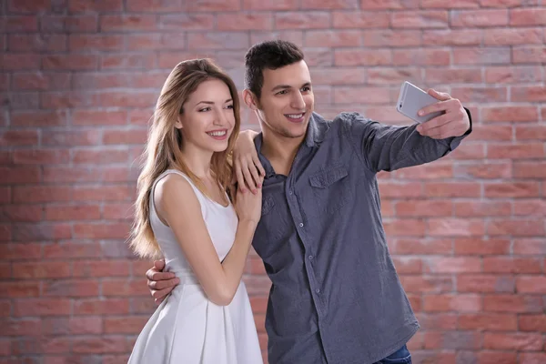年轻有吸引力的夫妇采取自拍用手机在砖墙背景上 — 图库照片