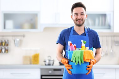 Plastik kova fırçalar, eldiven ve deterjanlar ile mutfakta tutan adam