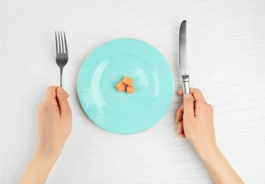 Bıçak ve çatal yanında havuç ile bir tabak Beyaz ahşap masa üzerinde tutan eller