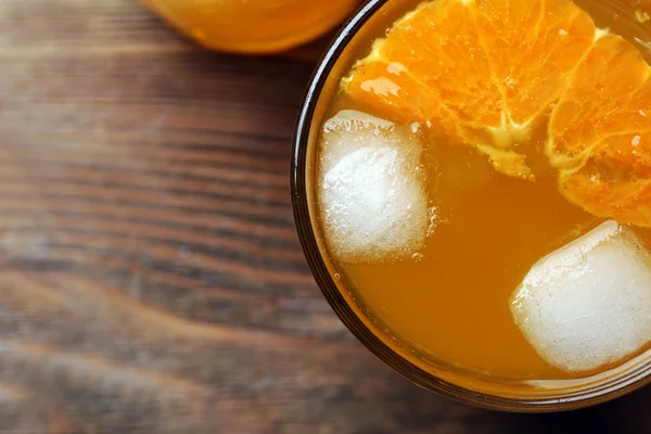 Vasos de zumo de naranja con bloques de hielo y rebanada de fruta sobre fondo de madera — Foto de Stock