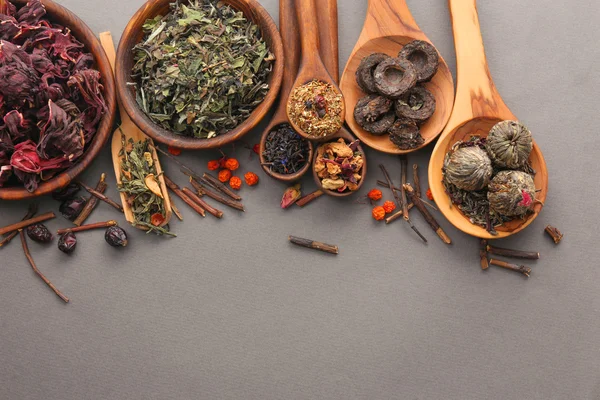 Variety of tea in wooden bowls and spoons on grey background, top view — Stock Photo, Image