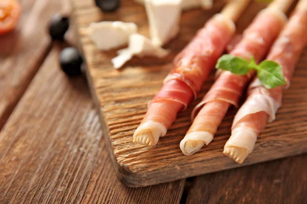 Brood stokken grissini met prosciutto-ham op een houten bord, close-up — Stockfoto