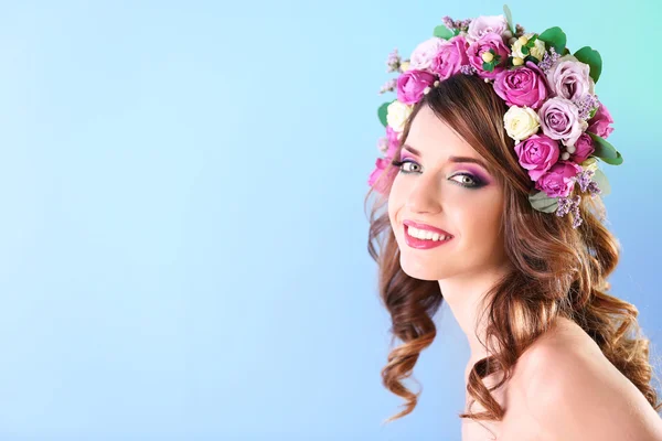 Hermosa mujer joven con diadema floral sobre un fondo azul — Foto de Stock