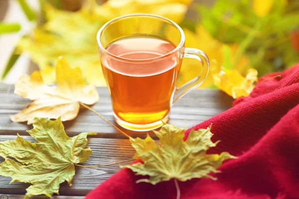 Taza de té con cuadros rojos y hojas de otoño sobre mesa de madera — Foto de Stock