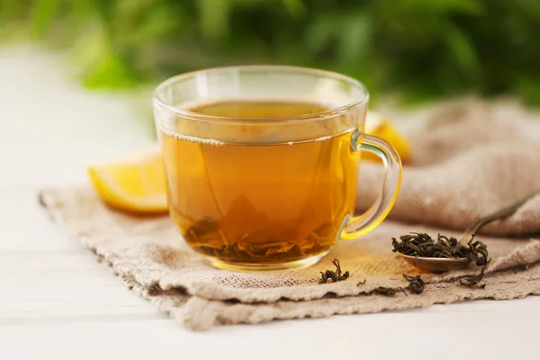 Glass cup of green tea with sliced lemon on wooden table with sackcloth closeup — Stock Photo, Image