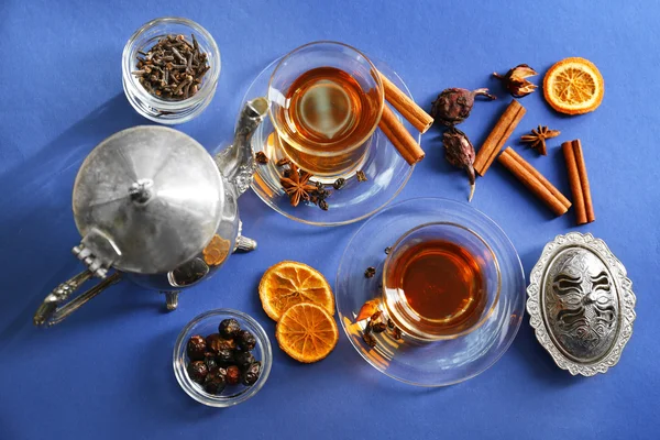 Tazze di tè e teiera in vetro con cannella e limone su sfondo blu, vista dall'alto — Foto Stock