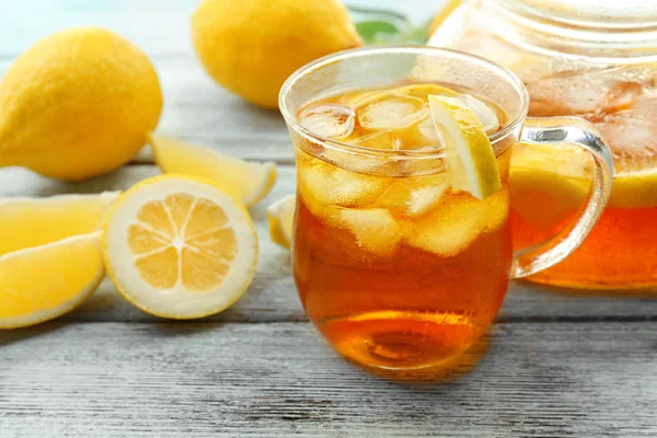 Bicchiere di tè al limone freddo e pentola sul tavolo di legno — Foto Stock