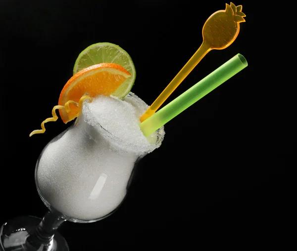 Hurricane glass with granulated sugar, cocktail tube and citrus slices on black background