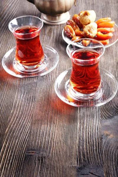 Černý se vaří čaj v skleněné poháry s východní sladkosti na dřevěný stůl — Stock fotografie