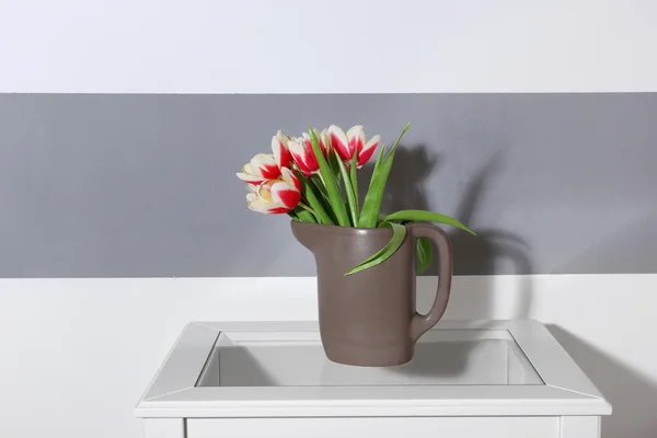 Bukett av brokiga tulpaner i kannan på vitt bord nära randig vägg — Stockfoto