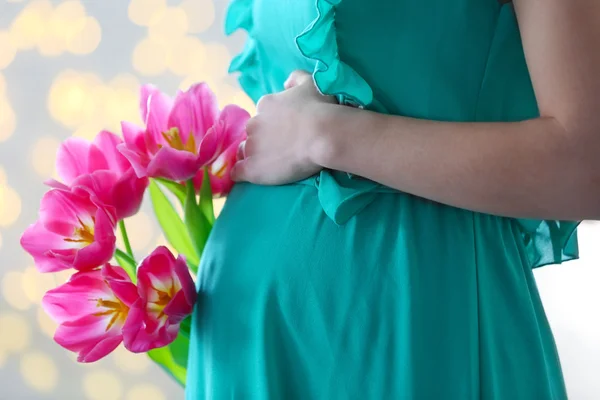 Zwangere vrouw in groene jurk met roze tulpen op glitter achtergrond — Stockfoto
