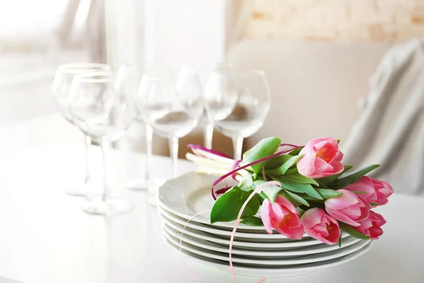 Букет розовых тюльпанов над тарелками на деревянном столе . — стоковое фото