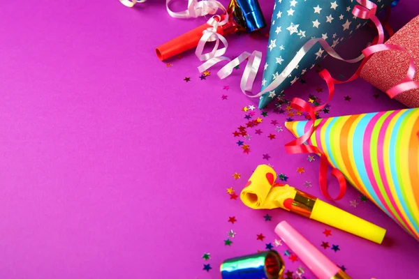 Birthday hats with serpentine streamer and noise makers on purple background — Stock Photo, Image