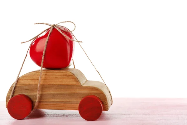 Wooden car with a red heart  tied to it on a pink wooden table over white background — Stock Photo, Image