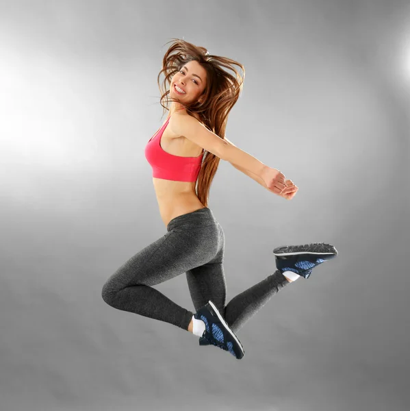 Młoda kobieta sportowy skoki na szarym tle — Zdjęcie stockowe