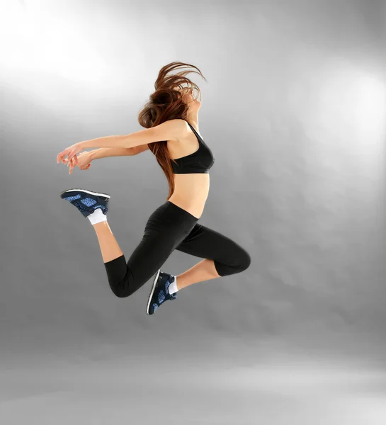 Young sporty woman jumping on grey background — Stock Photo, Image