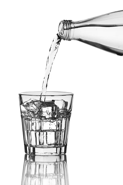 Наливаємо воду з пляшки в склянку з льодом на сірому фоні — стокове фото