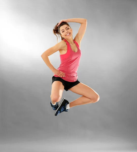 Jonge sportieve vrouw springen op grijze achtergrond — Stockfoto