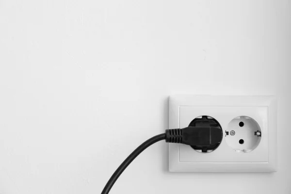 Conector de alimentación negro en zócalo contra fondo de pared blanco — Foto de Stock