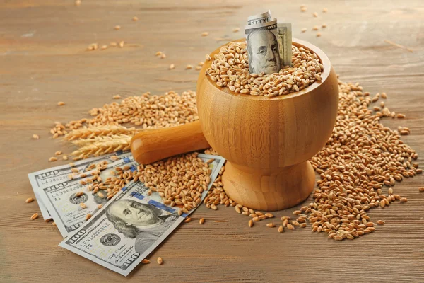 Dollar banknotes and wheat grains in bowl on wooden background. Agricultural income concept — Stock Photo, Image