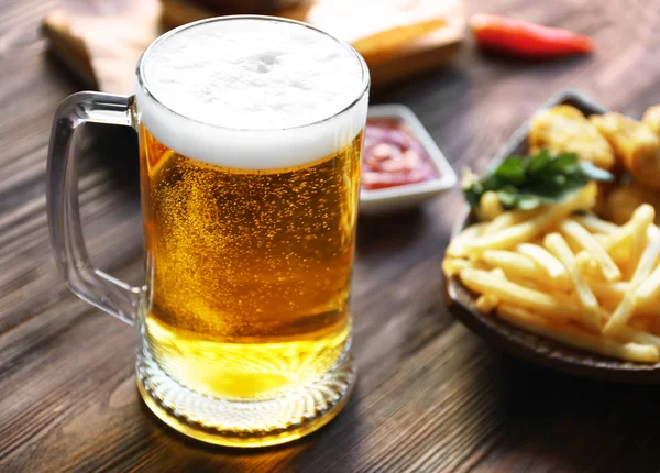 Glass mug of light beer with French fries on dark wooden table, close up — Stock Photo, Image