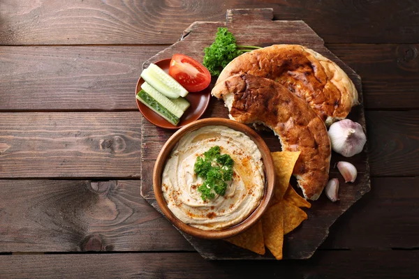 Fából készült tál ízletes hummus, chips, a lapos kenyér és a petrezselyemmel, a táblázat — Stock Fotó