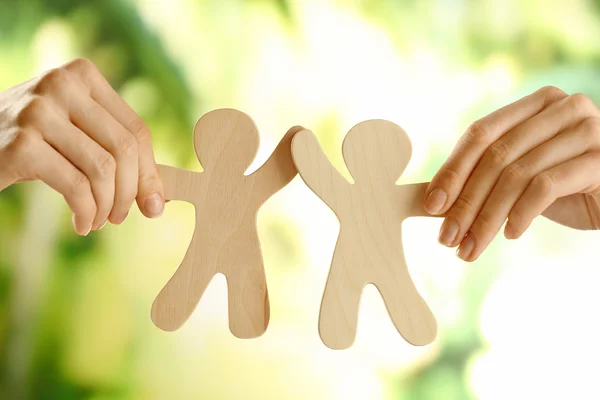 Hands holding a couple of wooden figures on green blurred background — Stock Photo, Image