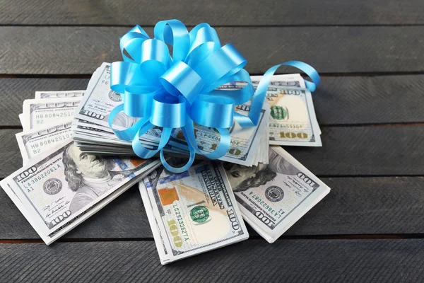 Pile of dollars with bow as gift on wooden background — Stock Photo, Image