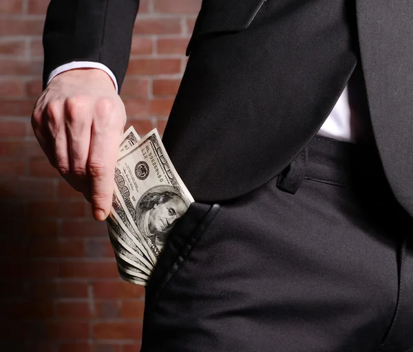 Man getting dollar banknotes out of suit pocket on brick wall background — Stock Photo, Image