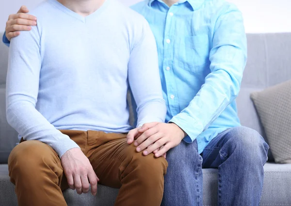 Dos homosexuales sentados en el sofá y tomándose de las manos — Foto de Stock