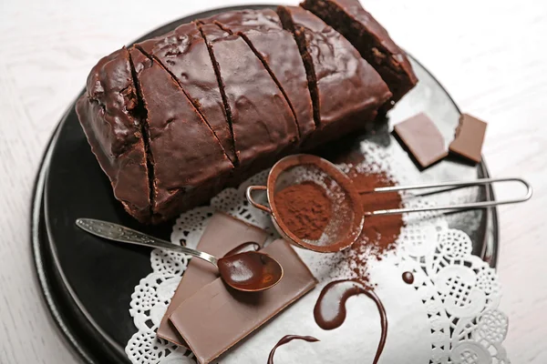 Bolo de chocolate fatiado com gelo e cacau em pó na assadeira sobre mesa branca — Fotografia de Stock