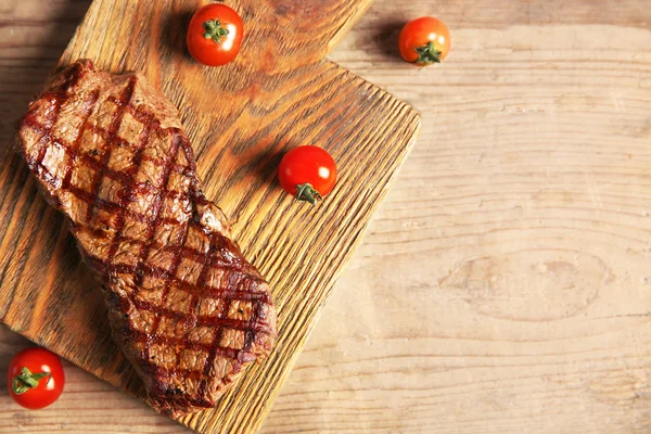 Grilled steak on cutting board with cherry tomatoes, closeup — Stock Photo, Image