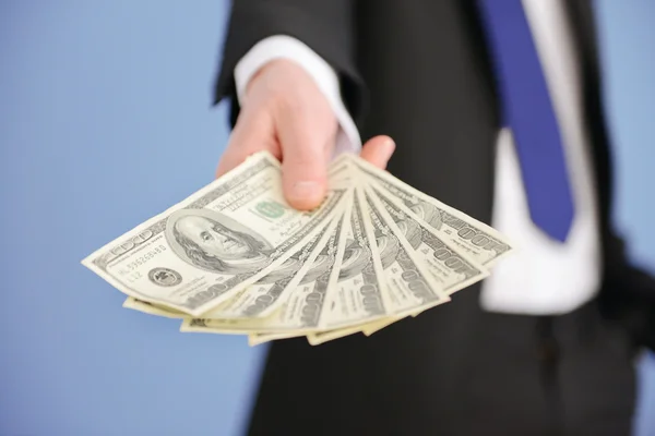 Man in a suit holding fan of dollar banknotes on blue background — Stock Photo, Image