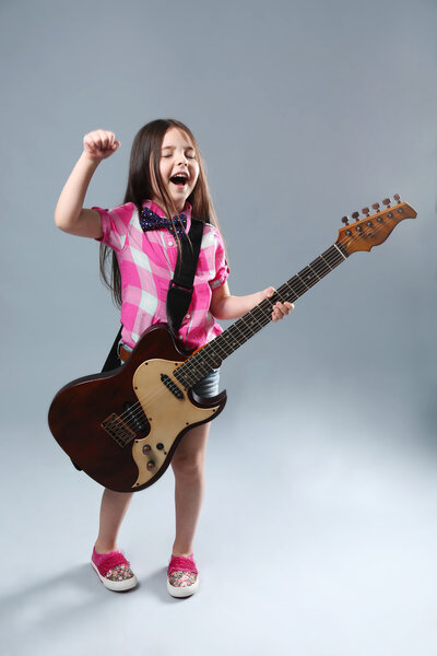 Девочка, играющая на гитаре на сером фоне
