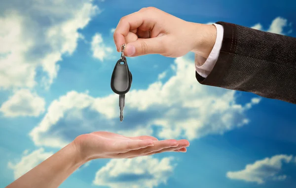 Male hand giving a car key to female hand on sky background