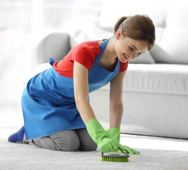 Junge Frau putzt Teppich im Zimmer — Stockfoto