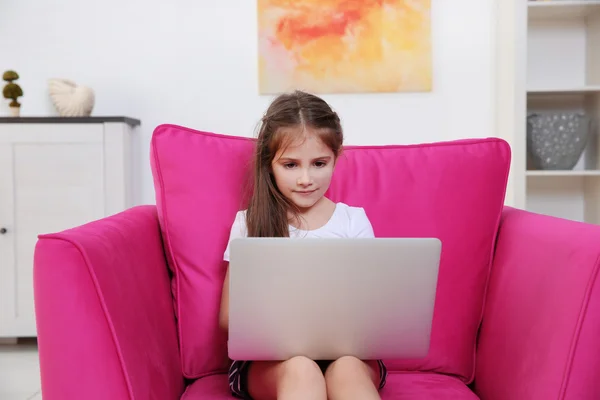 小女孩坐在粉红色的扶手椅上使用膝上型电脑 — 图库照片