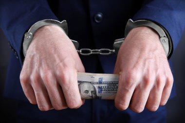 Ellerinde dolar banknotları tutan elleri kelepçeli bir adam.