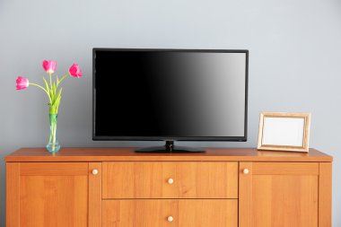 gri duvarının yakınında ahşap komodin üzerinde geniş ekran Tv