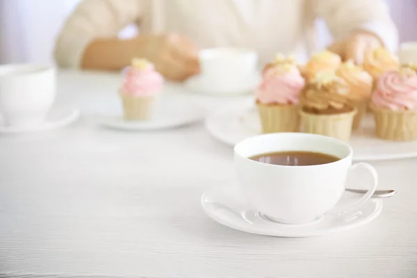 Female hands at the table with tea and cupcakes closeup — Stock Photo, Image